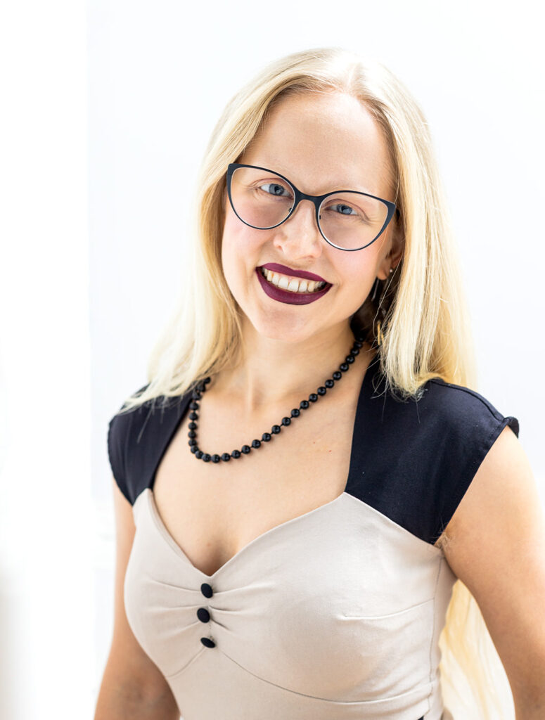 Somatic Therapist Crista Reid facing forward and smiling, wearing a black necklace and tan and black dress.