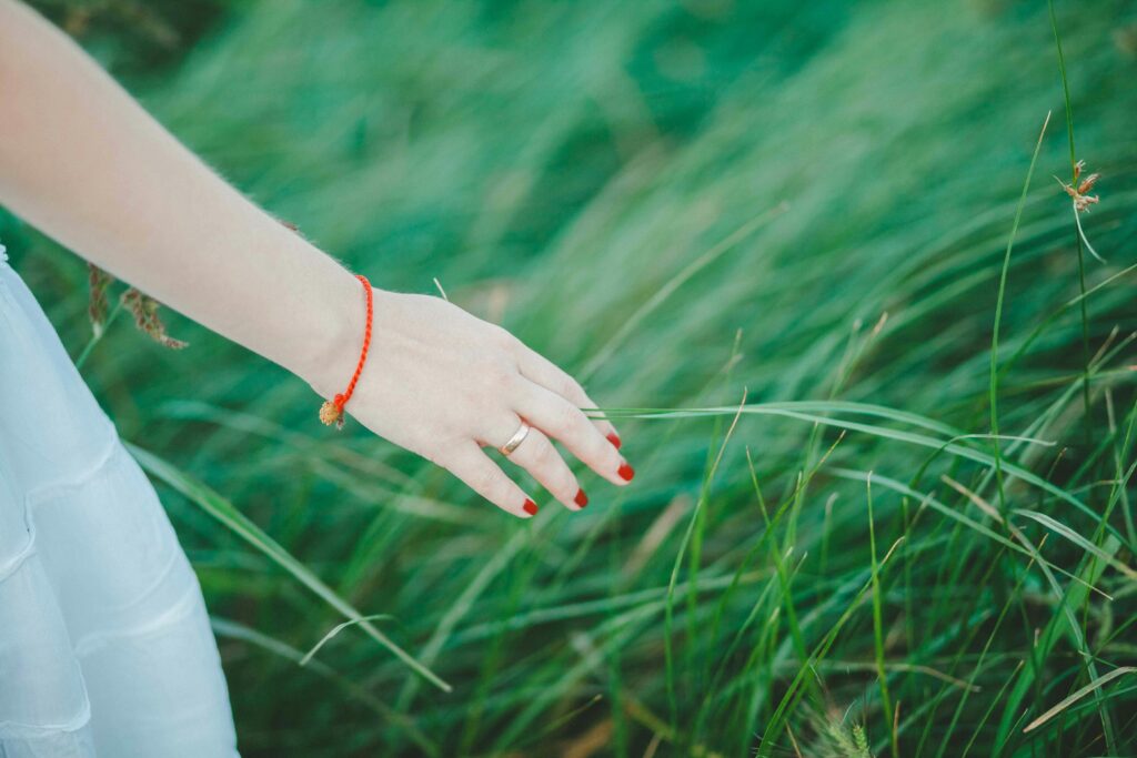 A woman's hand with red nails and bracelet gently touches lush green grass outdoors. sex therapy Colorado, somatic therapy Denver. mindfulness