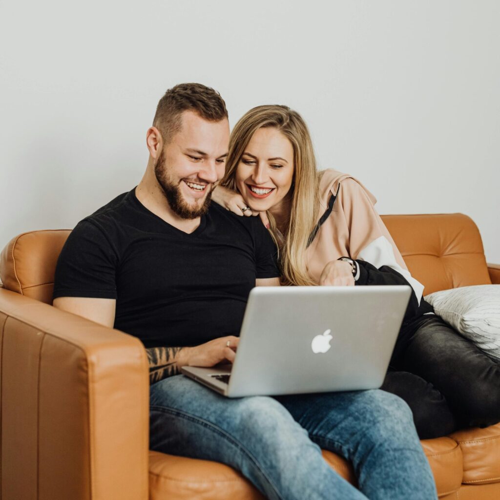 Happy couple sitting on a couch using a laptop, enjoying each other's company indoors.