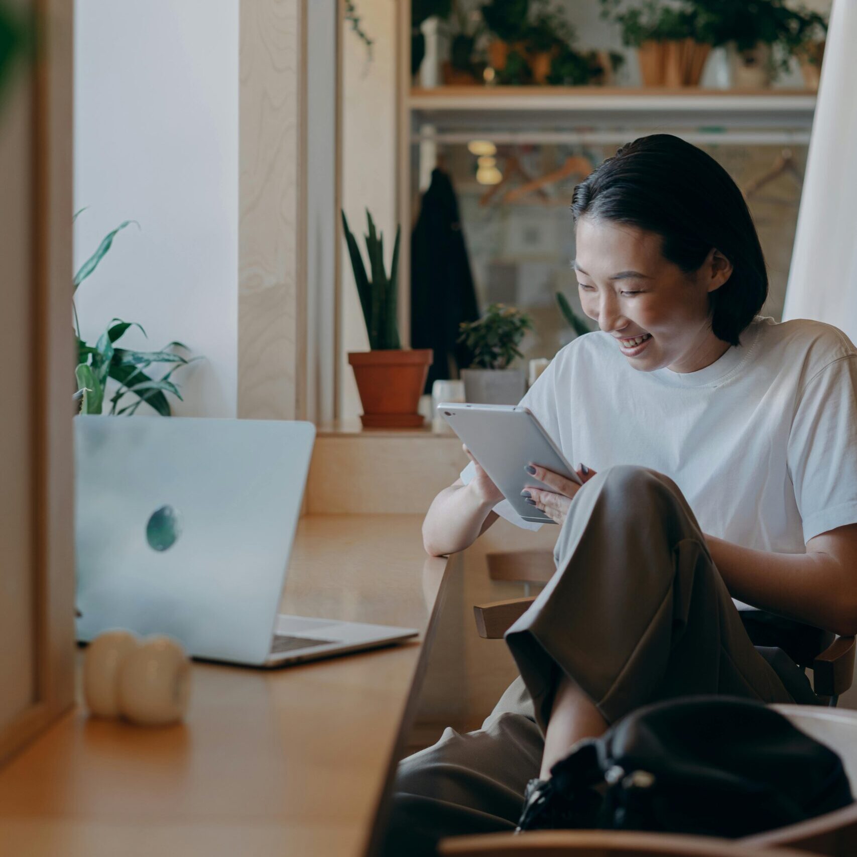 Asian woman enjoying digital tablet while working remotely in a cozy cafe setting.